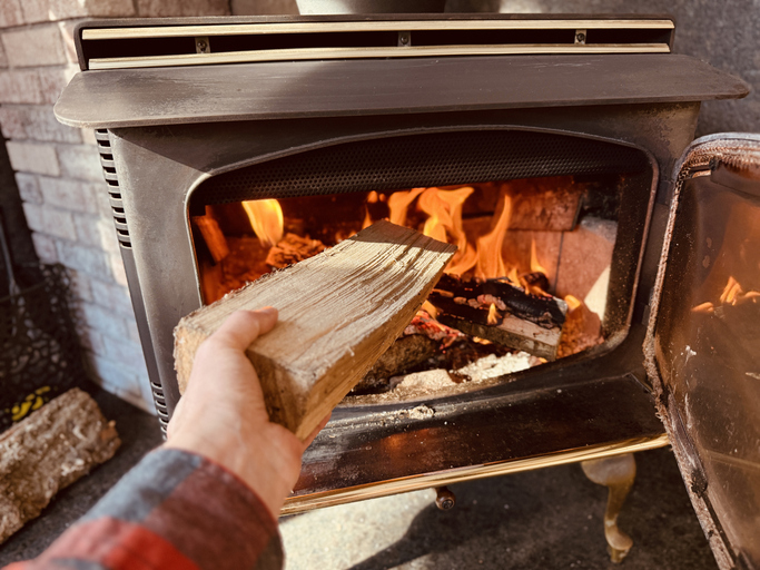 Hand adding a log to a burning fire inside a wood stove, providing warmth and comfort in a cozy indoor setting.