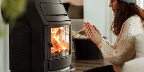 Person warming hands by a cozy indoor wood stove in winter attire.